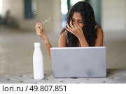A visibly distressed young woman sits in front of her open laptop, nervously holding her glasses as she expresses deep frustration, beautifully encapsulating the struggles of modern work life today. A Frustrated Woman Struggling to Work on Her Laptop While Holding Glasses in Her Hand. Стоковое фото, агентство Ingram Publishing / Фотобанк Лори