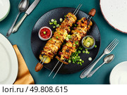Roasted or grilled bacon, meat skewers with roasted potatoes and sauce. Overhead view.. Summer cookout, meat and vegetables roast on skewers. Стоковое фото, агентство Ingram Publishing / Фотобанк Лори