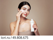 Young girl holds cotton pad while cleansing face with cosmetic milk. Skin care removal of makeup cleansing. Basic facial skin care. Стоковое фото, агентство Ingram Publishing / Фотобанк Лори