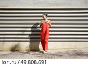 A stylish and fashionable woman poses confidently in a vibrant and eyecatching red dress, standing proudly against a modern textured wall, showcasing her contemporary style and elegant personality. A Stylish Woman Dressed in a Vibrant Red Dress Posing in Front of a Textured Wall. Стоковое фото, агентство Ingram Publishing / Фотобанк Лори