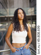 In a vibrant urban setting, a confident young woman with curly hair embodies modern youth culture through her distinct style and charm, reflecting a contemporary vibe that is engaging and captivating. A Confident Young Woman Posing Gracefully in a Modern Urban Setting Under Bright Daylight. Стоковое фото, агентство Ingram Publishing / Фотобанк Лори