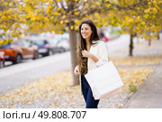 A cheerful young woman enjoys shopping in a beautiful park filled with vibrant autumn leaves. She holds a stylish bag and radiates happiness with her infectious smile on this lovely day. A young woman happily shopping in a vibrant autumn park filled with colorful leaves. Стоковое фото, агентство Ingram Publishing / Фотобанк Лори