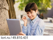 A joyful and enthusiastic young woman happily interacts with her tablet while outdoors, showcasing her excitement and engagement in a lively, vibrant, and colorful natural setting. A joyful and excited young woman is happily engaged with her tablet in a beautiful outdoor setting, Стоковое фото, агентство Ingram Publishing / Фотобанк Лори