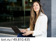 A young woman smiles confidently using her laptop outdoors in a vibrant urban setting, blending professionalism with casual style, illustrating the intersection of technology and creativity. Confident Woman Engaged in Productive Work on Laptop While Enjoying the Outdoors. Стоковое фото, агентство Ingram Publishing / Фотобанк Лори