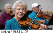 Seniors joyfully playing violins in orchestra practice. Стоковое AI-изображение, AI-художник Юрий Поздников / Фотобанк Лори