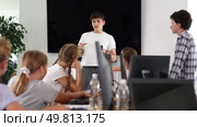 Young male teacher making explanation to children sitting at computer table in IT training room. Стоковое видео, видеограф Яков Филимонов / Фотобанк Лори