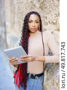 A stylish young woman confidently holds a tablet, showcasing her personality against a textured wall that adds depth in an urban environment, capturing the essence of contemporary life. A Confident Young Woman Holding a Tablet while Posing in a Vibrant Urban Background Scene. Стоковое фото, агентство Ingram Publishing / Фотобанк Лори