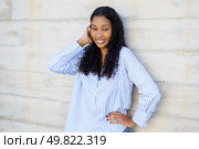 A stylish, fashionable young woman with curly hair smiles confidently against a solid concrete wall, radiating charm and embodying the essence of youthfulness and a vibrant, lively personality. SelfAssured Young Woman Posing Gracefully Against a Contemporary Concrete Wall Background. Стоковое фото, агентство Ingram Publishing / Фотобанк Лори