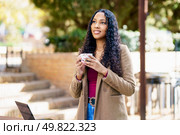 A young woman stands outdoors in a beautiful environment, confidently holding a coffee cup, radiating joy and positivity, immersed in a moment of contemplation, surrounded by serenity. A Confident Woman Happily Enjoys A Cup Of Coffee While Outdoors In A Relaxing Setting. Стоковое фото, агентство Ingram Publishing / Фотобанк Лори