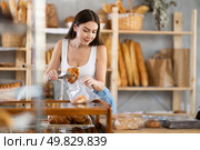 Female shopper selects and places fresh croissants in plastic bag at bakery. Стоковое фото, фотограф Яков Филимонов / Фотобанк Лори