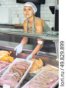 Positive young saleswoman demonstrating container with sausages in butcher shop. Стоковое фото, фотограф Яков Филимонов / Фотобанк Лори
