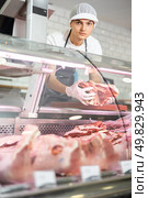 Positive young salesman demonstrating piece of meat in butcher shop. Стоковое фото, фотограф Яков Филимонов / Фотобанк Лори