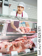 Positive young salesman demonstrating piece of meat in butcher shop. Стоковое фото, фотограф Яков Филимонов / Фотобанк Лори
