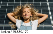 A young blonde girl is laying on a black solar panel. Стоковое AI-изображение, AI-художник Ярославский Максим / Фотобанк Лори