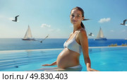 A pregnant woman enjoys tranquility by the clear waters of the ocean against a backdrop of flying seagulls and turquoise waves. Стоковое AI-видео, аниматор Оксана Медведева / Фотобанк Лори