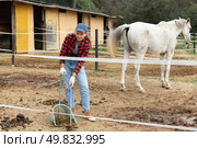 Girl worker scoops horse droppings into shovel and cleans up cattle. Стоковое фото, фотограф Яков Филимонов / Фотобанк Лори
