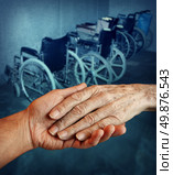Disabled and Handicapped elderly medical health care concept with a young person holding and giving a helping hand to an old elderly grandparent with a group of wheelchairs in the background. Стоковое фото, агентство Ingram Publishing / Фотобанк Лори