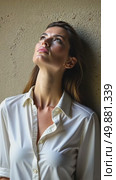A caucasian young woman in a white blouse standing confidently with her arm scratches and ruffles her hair against a textured stone wall, soft lighting enhancing. Стоковое AI-видео, аниматор Sergey Grishin / Фотобанк Лори