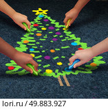 Community Christmas concept as a group of multicultural children drawiing a decorated pine tree on the floor using chalk  as a winter holiday symbol for cooperation and working together to celebrate a time of giving. Стоковое фото, агентство Ingram Publishing / Фотобанк Лори
