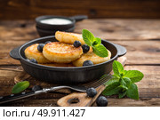 Delicious cottage cheese pancakes or syrniki with fresh blueberry in cast-iron pan on dark wooden rustic background, above view. Tasty breakfast. Стоковое фото, агентство Ingram Publishing / Фотобанк Лори