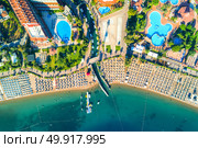 Aerial view of transparent turquoise sea, beautiful sandy beach with colorful chaise-lounges, boats, green trees, pool, hotels, buildings at sunset in Icmeler, Turkey. Summer landscape. Top view.. Aerial view of Icmeler, Turkey. Стоковое фото, агентство Ingram Publishing / Фотобанк Лори