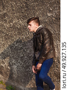 stylish young brunet in leather jacket standing near wall. Стоковое фото, агентство Ingram Publishing / Фотобанк Лори