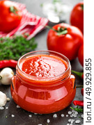 Tomato paste, puree in glass jar and fresh tomatos on dark background. Hot vegetable sauce with chili pepper ant tomatoes. Стоковое фото, агентство Ingram Publishing / Фотобанк Лори