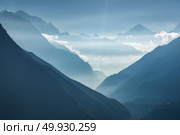 Majestic view of silhouettes of mountains and low clouds at sunset in Nepal. Landscape with high rocks of Himalayan mountains, beautiful blue sky and sun rays. Amazing Himalayas. Nature background . Majestic view of silhouettes of mountains and low clouds at sunset. Стоковое фото, агентство Ingram Publishing / Фотобанк Лори