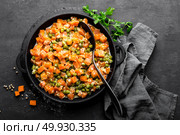 Carrot braised with fresh green peas in creamy milk sauce in stewpan, vegetable saute on black background, top view. Стоковое фото, агентство Ingram Publishing / Фотобанк Лори