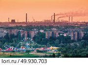 Amusement park with Ferris wheel and buildings on the background of metallurgy plant with smog at sunset. Ecology problems, atmospheric pollutants. Pipes with smoke. Heavy industry factory. Steel mill. Стоковое фото, агентство Ingram Publishing / Фотобанк Лори