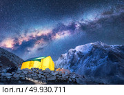 Milky Way, yellow glowing tent and mountains. Amazing scene with himalayan mountains, starry sky at night in Nepal. Rocks with snowy peak and sky with stars. Night landscape with milky way. Space. Стоковое фото, агентство Ingram Publishing / Фотобанк Лори