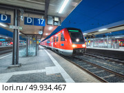High speed train on the railway station at night in Nuremberg, Germany. Modern intercity train on the railway platform with illumintain. Commuter red train on railroad. Passenger transportation. Dusk. High speed train on the railway station at night. Стоковое фото, агентство Ingram Publishing / Фотобанк Лори