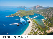 Airplane is flying over islands and sea at sunrise in summer. Landscape with white passenger airplane, seashore, mountains, sky, and blue water. Blue passenger aircraft. Travel and resort. Tourism. Blue airplane is flying over islands and sea at sunrise in summer. Стоковое фото, агентство Ingram Publishing / Фотобанк Лори