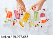 Fruit berry ice lolly on ice cubes. A woman’s hand decorates ice cream with pieces of fresh fruit fruit. Flat lay. The woman’s hands decorate the ice cream on a stick with bits of juicy fruit. Summer dessert. Flat lay. Стоковое фото, агентство Ingram Publishing / Фотобанк Лори