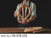 Delicious freshly baked fougas bread in the hands of a man on a black background. Baker’s hands hold fougas bread. Стоковое фото, агентство Ingram Publishing / Фотобанк Лори