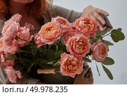 Hands of a red-haired girl holding a vase with delicate fresh pink roses around a gray background. A gift for Mother’s Day. Beautiful pink flowers are holding female hands on a gray background. Happy Valentine’s Day. Стоковое фото, агентство Ingram Publishing / Фотобанк Лори