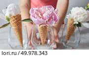 Woman hold a glass cup with beautiful pink flower pion in her hand above gray stone table.. Glass vase in a woman hands with gentle pink and white peony flowers on a gray concrete table. Стоковое фото, агентство Ingram Publishing / Фотобанк Лори