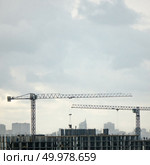 Panoramic photo from the drone of building under construction with two tower cranes against a gray cloudy sky.. Construction cranes against the background cityscape and cloudy sky. Aerial photo from the drone. Стоковое фото, агентство Ingram Publishing / Фотобанк Лори