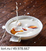 Splashes of milk yogurt in different directions, ripe peach fruit falls into a ceramic bowl. Preparation of a delicious healthy breakfast.. Pieces of ripe fresh peach fell in a ceramic bowl with a splash of yoghurt on a wooden table. Стоковое фото, агентство Ingram Publishing / Фотобанк Лори
