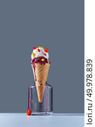 A delicious dessert in a waffle cone with red and yellow pills and lollipops stands in a glass jar on gray background. The concept of summer catarrhal diseases and their treatment with place for text.. The waffle cone stands in glass jar with a ball of berry and vanilla ice cream with red and yellow pills and a lollipops on a dark gray background. Copy space. Стоковое фото, агентство Ingram Publishing / Фотобанк Лори