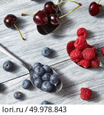 Mix of fresh organic berries - blueberries, cherries, raspberries on a gray wooden background. Top view.. Delicious sweet berries on a spoon gray wooden background. Flat lay. Concept of vegetarian eating. Стоковое фото, агентство Ingram Publishing / Фотобанк Лори