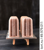 Natural chocolate ice cream popsicle in plastic forms presented on a black wooden table with a copy of the space for text. Homemade chocolate ice cream lolly in a plastic mold, on a black wooden background with copy space. Стоковое фото, агентство Ingram Publishing / Фотобанк Лори