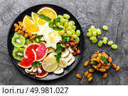 Healthy vegetarian bowl dish with fresh fruits and nuts. Plate with raw apple, orange, grapefruit, banana, kiwi, lemon, grape, almond, hazelnut and cashew nuts. Healthy balanced eating. Стоковое фото, агентство Ingram Publishing / Фотобанк Лори