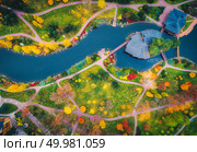 Aerial view of amazing autumn park with pond in europe at sunset. Landscape with trees with colorful leaves, buildings, field with green grass and paths in fall. Scenery. Top view of forest. Nature. Стоковое фото, агентство Ingram Publishing / Фотобанк Лори