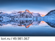 Beautiful snow covered mountains and colorful sky reflected in water at dusk. Winter landscape with sea, snowy rocks, blue sky, reflection, at sunset. Lofoten islands, Norway at twilight. Nature. Стоковое фото, агентство Ingram Publishing / Фотобанк Лори