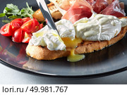 The knife cuts the Eggs Benedict on toasted bread with ham, tomatoes and sauce. Eggs Benedict on toasted with ham and sauce. Стоковое фото, агентство Ingram Publishing / Фотобанк Лори