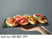 delicious variety of Italian bruschetta on a ceramic tray holds the hand of man. delicious variety of Italian bruschetta on a ceramic tray. Стоковое фото, агентство Ingram Publishing / Фотобанк Лори