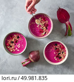 The girl’s hand puts oatmeal in a plate with freshly prepared beetroot smoothies with raspberries and currants on a gray concrete background. Top view. Concept of diet and vegetarian food. A healthy smoothie with oatmeal, berries and beets on a gray concrete background, the girl’s hand pours flakes of oatmeal into a plate. Top view. Стоковое фото, агентство Ingram Publishing / Фотобанк Лори