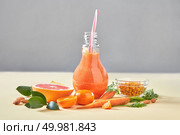 Vegetarian colorful orange cocktail from organic vegetables, fruits and berries on a paper background with copy space. Concept of natural organic healthy food.. Homemade orange smoothies with carrot, grapefruits, sea buckthorn, almonds in glass bottle on a yellow paper background. Стоковое фото, агентство Ingram Publishing / Фотобанк Лори