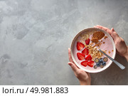 Female hands hold a plate of fresh yoghurt, berries and homemade granola on a gray concrete background with a copy space. Healthy breakfast. Top view. Homemade granola with yogurt and berries in a plate. Female hands hold a plate on a gray concrete background. Copy space for text. Top view. Стоковое фото, агентство Ingram Publishing / Фотобанк Лори